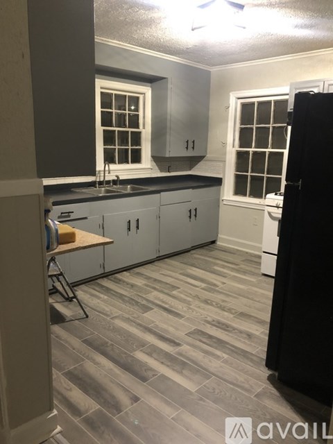 A kitchen with a black refrigerator and grey cabinets.