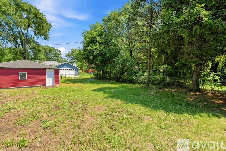 A red building with a white door is surrounded by trees and grass.