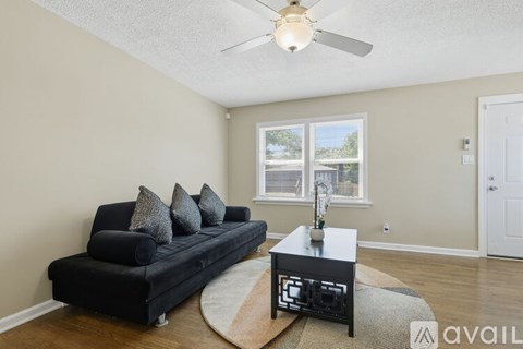 A living room with a black couch and a ceiling fan.