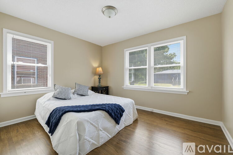 A bedroom with a bed, nightstand, and two windows.