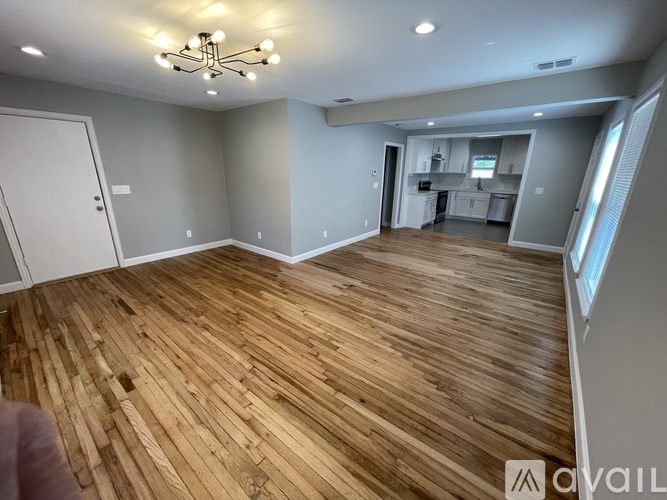 A spacious room with wooden flooring and a kitchen area in the background.