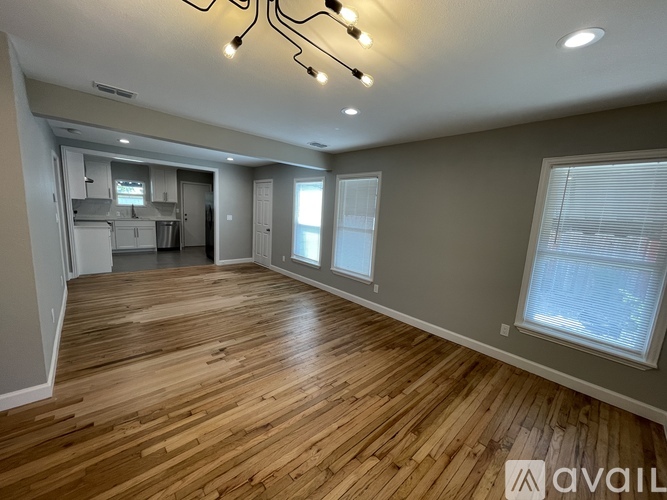 A spacious room with wooden flooring and a kitchen area in the background.
