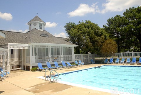 A pool with blue chairs and a white building with a clock tower in the background.