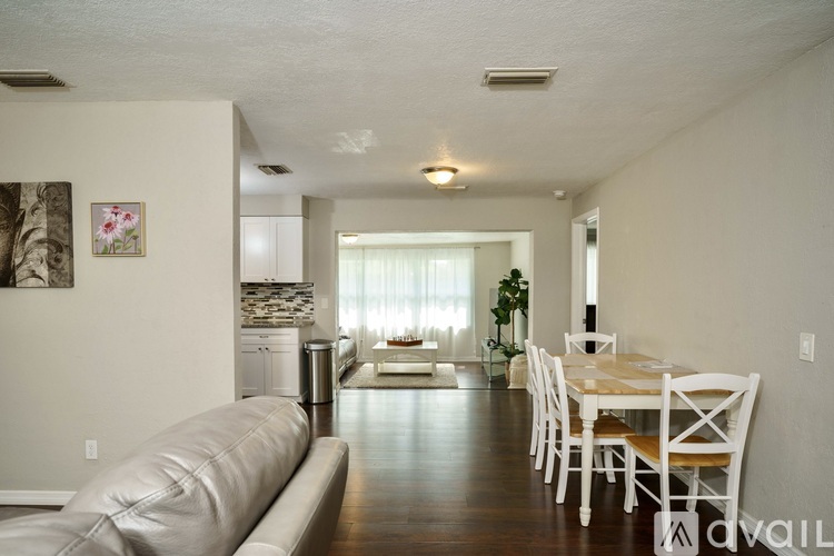 A living room with a couch, a dining table and chairs, and a kitchen area in the background.