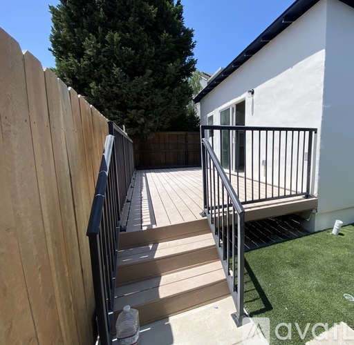 A wooden deck with a metal railing and steps leading to a white building.