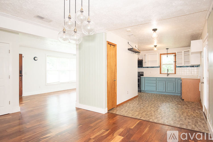 A living room with a rug on the floor and a kitchen area in the background.