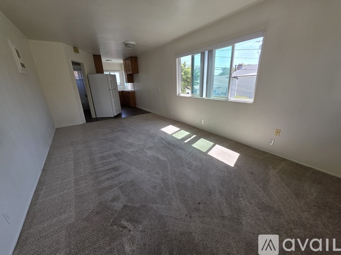 A spacious empty room with a carpeted floor and a refrigerator in the corner.