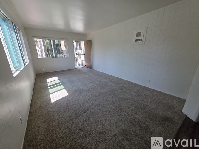 A spacious room with a carpeted floor and a window on the left side.