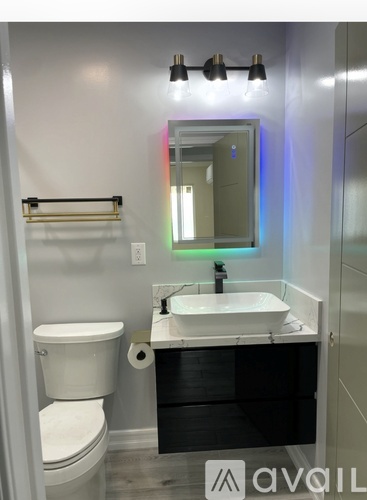 A bathroom with a toilet, sink, mirror, and lights.