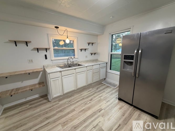 A kitchen with a refrigerator, sink, and wooden flooring.