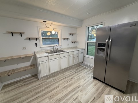A kitchen with a refrigerator, sink, and wooden flooring.