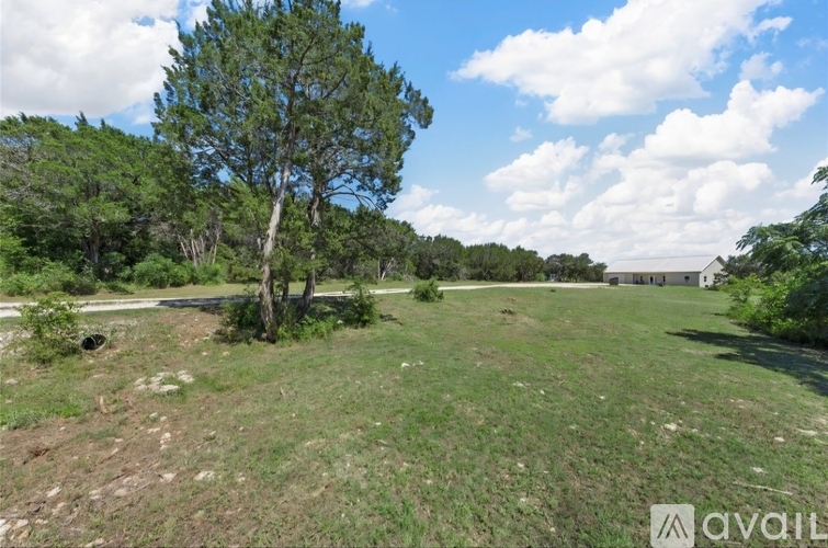 A grassy field with a tree and a house in the distance.