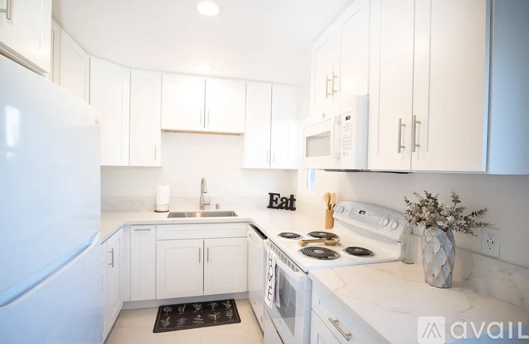 A kitchen with white cabinets and appliances, a sink, and a refrigerator.