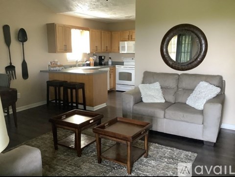 A living room with a grey couch and a round mirror on the wall.