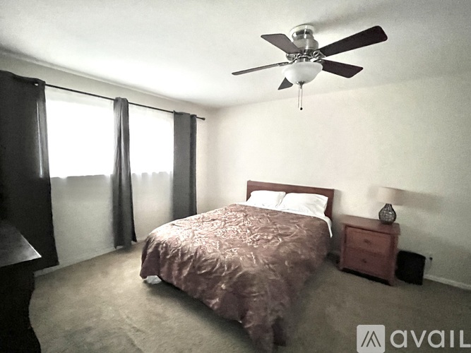 A bedroom with a bed, nightstand, and window with curtains.