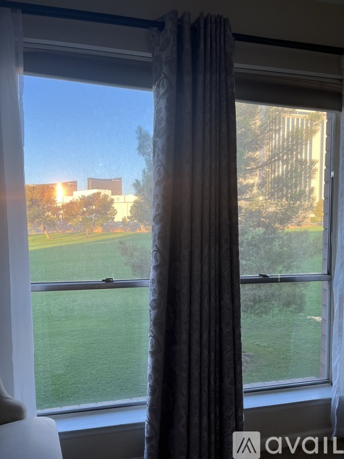 A window with a view of a green field and buildings outside.
