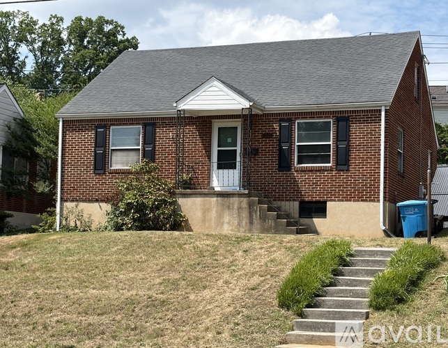 A small brick house with a front porch and a blue trash can.