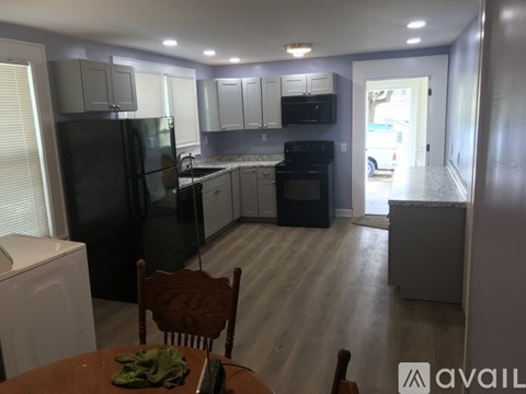 A kitchen with a black refrigerator, white washing machine, wooden chairs and a table with a green cloth on it.