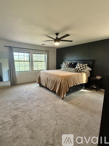 A bedroom with a bed, carpet, and a ceiling fan.