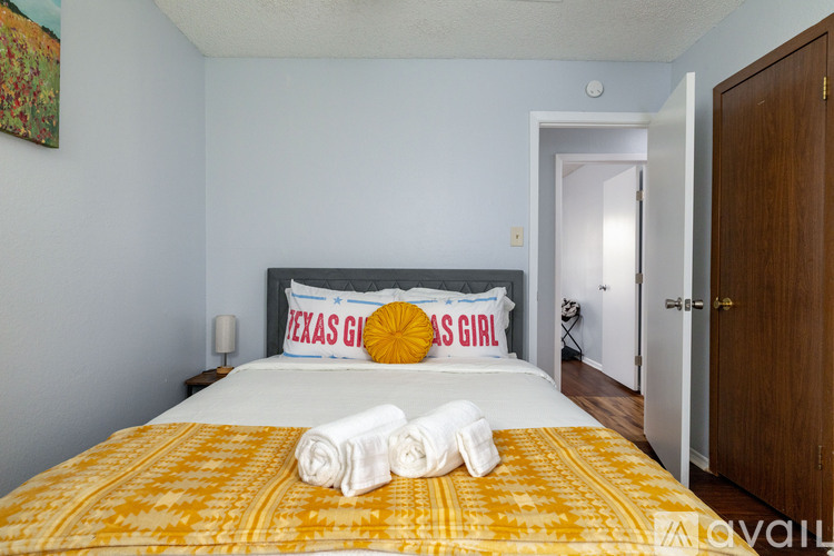 A bedroom with a bed covered in a yellow and white comforter and two pillows with the words "Texas Girl" on them.
