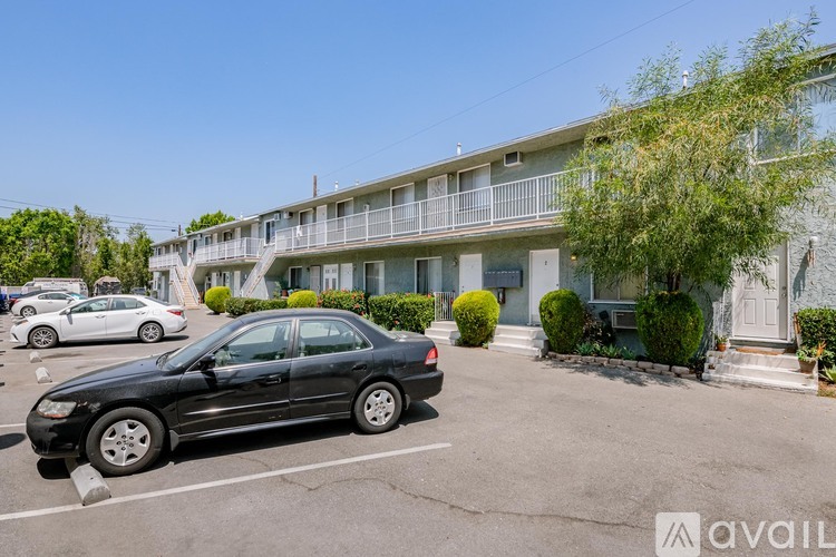 A black car is parked in a parking lot in front of a building with balconies.