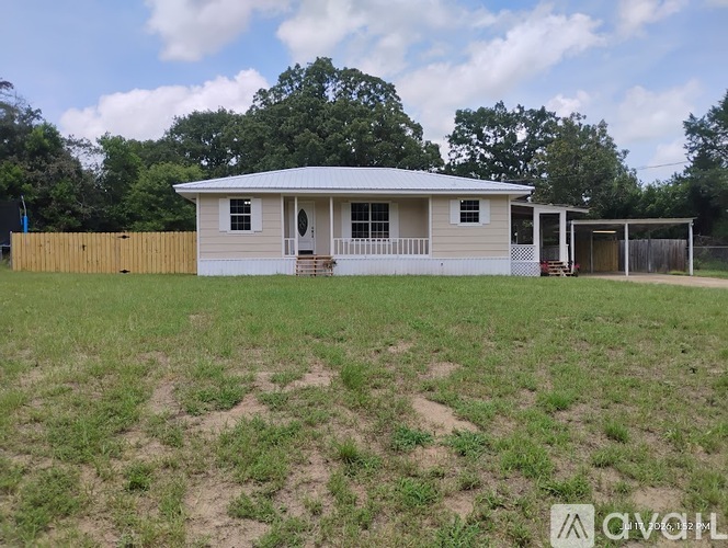A white house with a porch and a covered patio is surrounded by a grassy field.