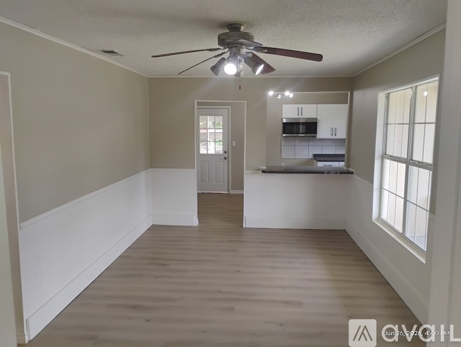 A spacious room with a ceiling fan and a kitchen area in the background.