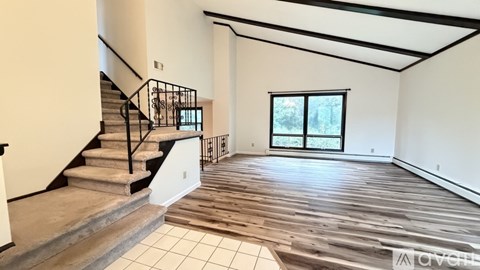 A spacious room with wooden flooring and a staircase with a metal railing.