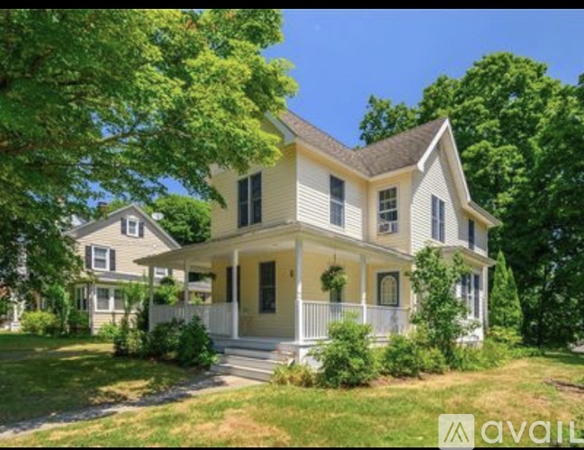 A two-story house with a front porch is surrounded by greenery.