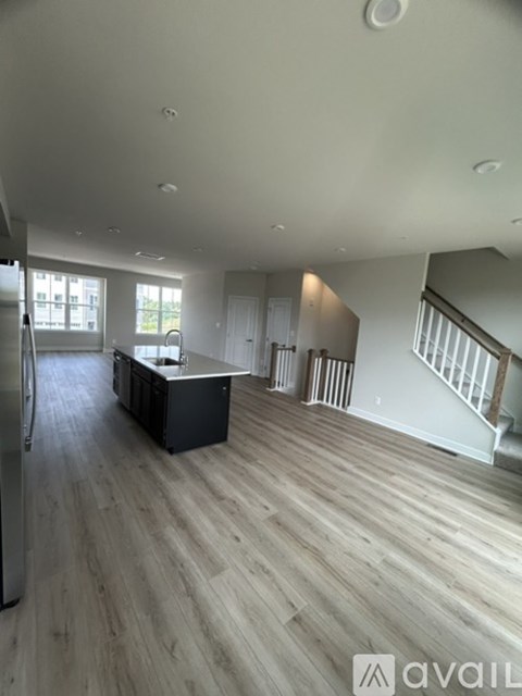 A spacious living room with wooden flooring and a staircase leading to another level.