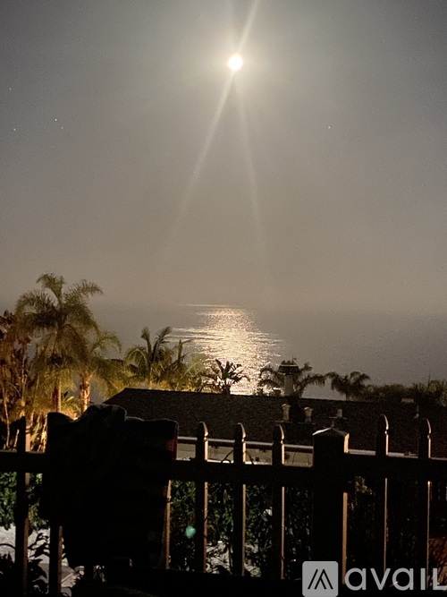 A bright moon shines over a body of water with a house and trees in the foreground.