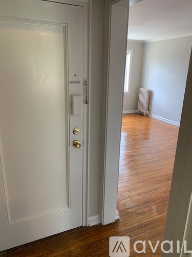 A white door with a brass handle is open to a room with a wood floor and a radiator.