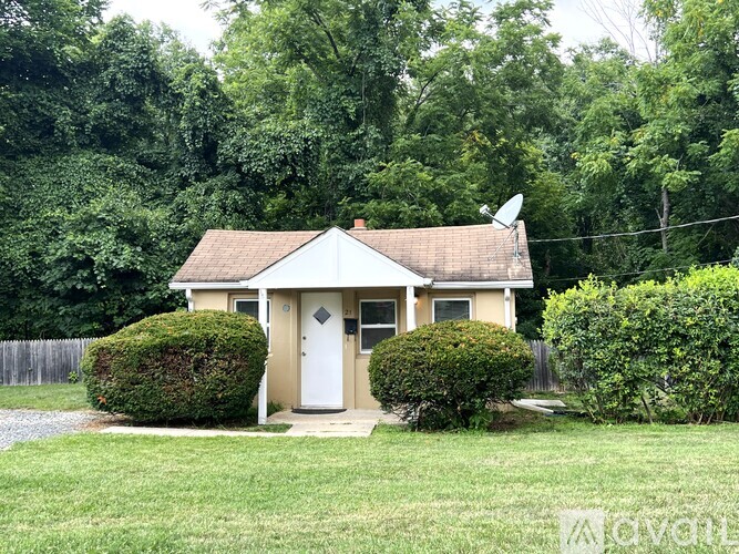 A small house with a white door is surrounded by greenery.