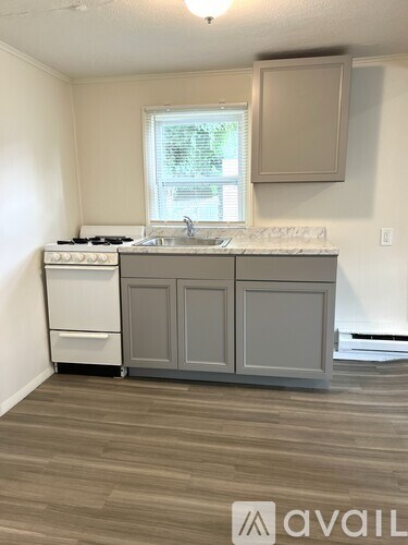 A kitchen with a white stove top oven and a white sink with a window above it.
