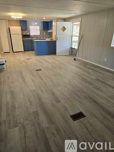 A room with wooden flooring and a kitchen area in the background.