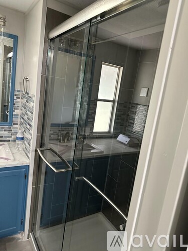 A modern bathroom with a glass shower door and a blue cabinet.