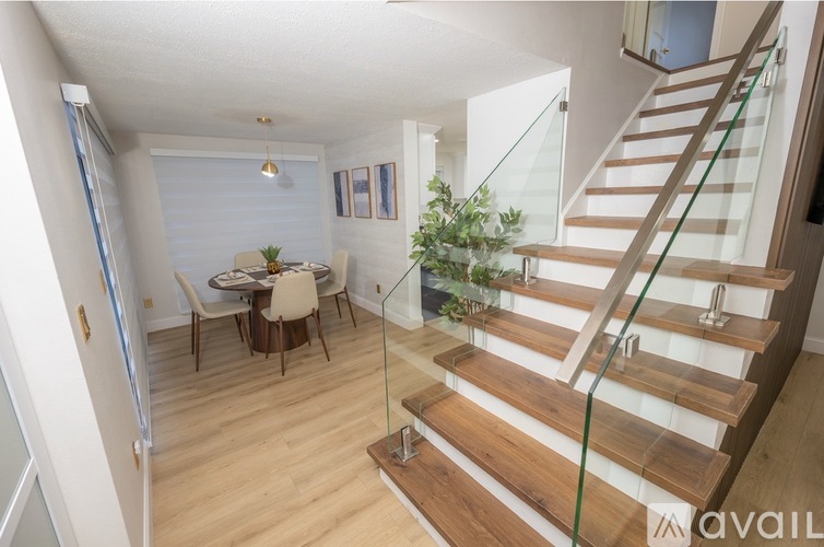 A wooden staircase with glass railings leads to a dining area with a table and chairs.