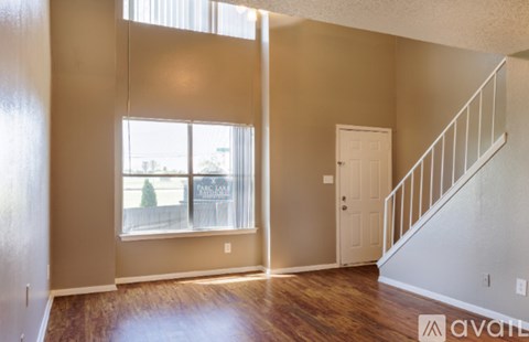 A room with a staircase and a window showing a view of a fence and trees.