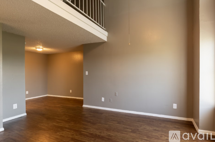 A spacious room with wooden floors and a staircase on the left side.
