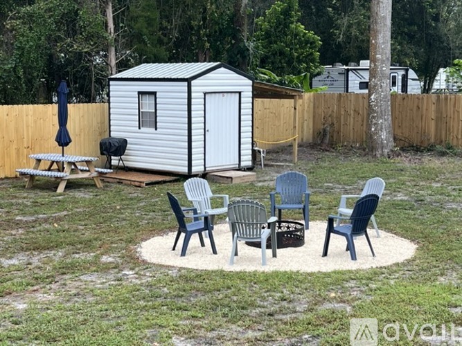 A white trailer is parked in a backyard with a picnic table and chairs.