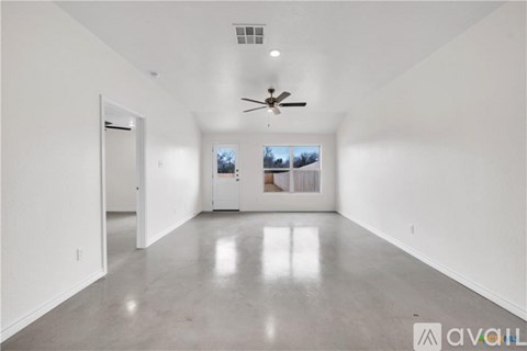 A spacious room with a ceiling fan and a view of the outdoors through the windows.