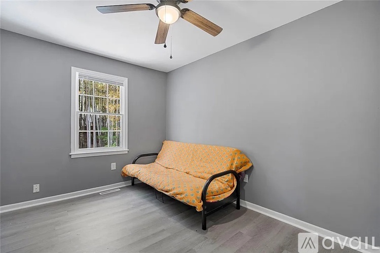A room with a ceiling fan and a window with a view of trees.