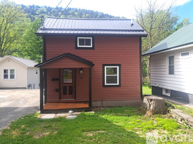 A red house with a brown door and windows is surrounded by green grass.