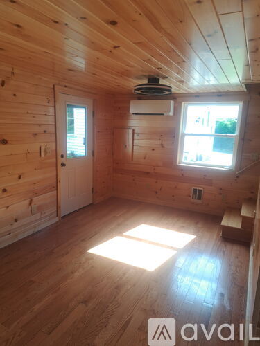 A room with wooden walls and ceiling, a window, and a door.