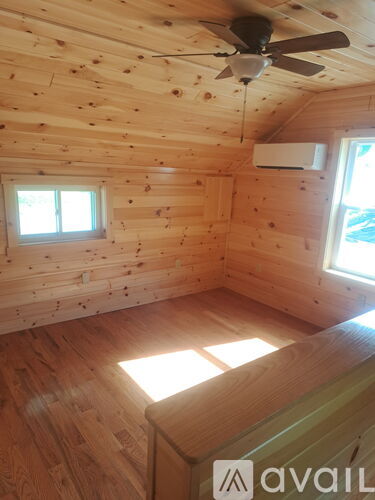 A wooden room with a ceiling fan and two windows.