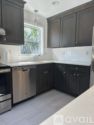 A kitchen with black cabinets and a stainless steel dishwasher.