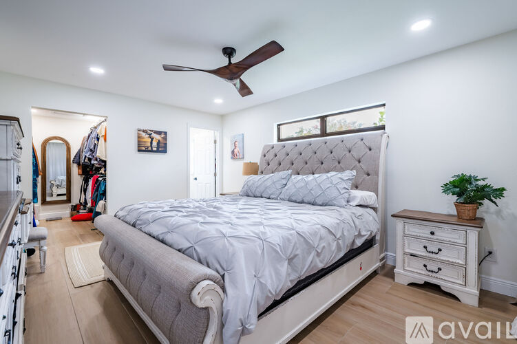 A well-lit bedroom with a large bed, a ceiling fan, and a small nightstand with a plant on it.