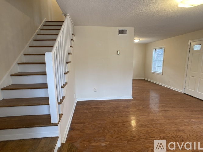 A spacious room with wooden floors and a staircase leading to the upper level.