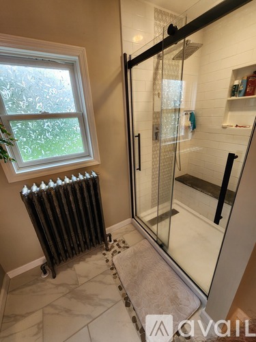 A bathroom with a window, a radiator, and a glass shower door.