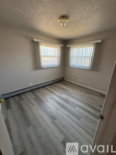 A room with grey wooden flooring and two windows with white curtains.
